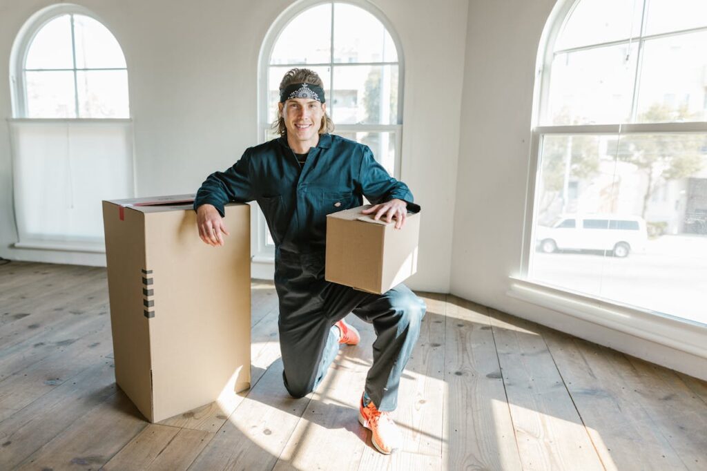 A mover in a coverall preparing boxes for relocation in a sunlit apartment.